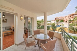 A balcony with wicker furniture, a glass table, and a view of a residential area.