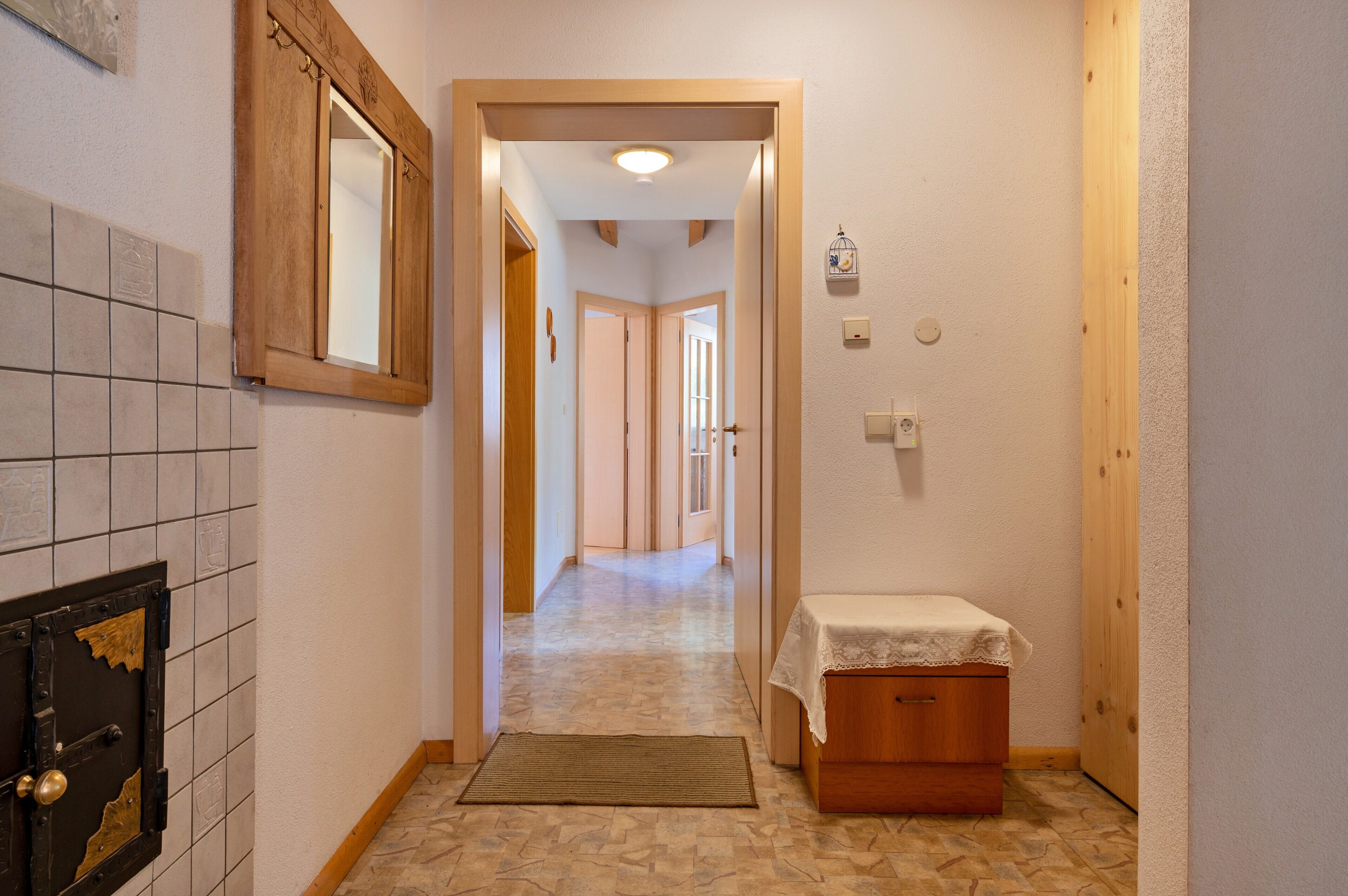 A narrow hallway with a tiled floor, a wooden door frame, a small table with a white cloth, and a light fixture on the ceiling.
