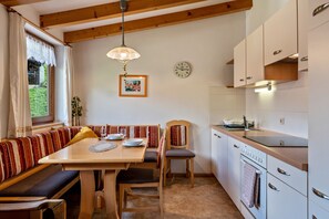 Une cuisine chaleureuse avec des bancs en bois, une table à manger, une horloge et une fenêtre avec des rideaux.