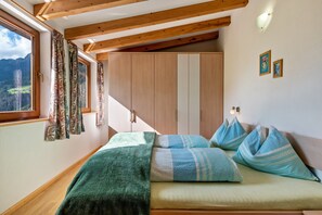 Un dormitorio con cama, ventana con cortinas, vigas de madera y un armario.