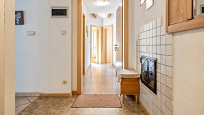 Un pasillo con suelo de baldosas, un banco, una caja fuerte en la pared y una puerta que da a otra habitación.