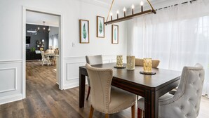 Un coin repas avec une table en bois foncé, des chaises recouvertes d’un tissu beige et un lustre.
