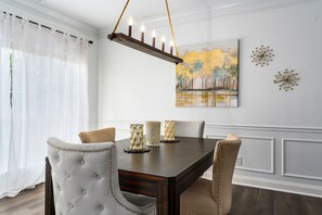Un comedor con una mesa de madera oscura, sillas capitonadas y una lámpara de araña.
