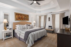 Un dormitorio con una cama grande, una mesita de noche con lámpara, un cuadro en la pared y un televisor sobre un mueble.