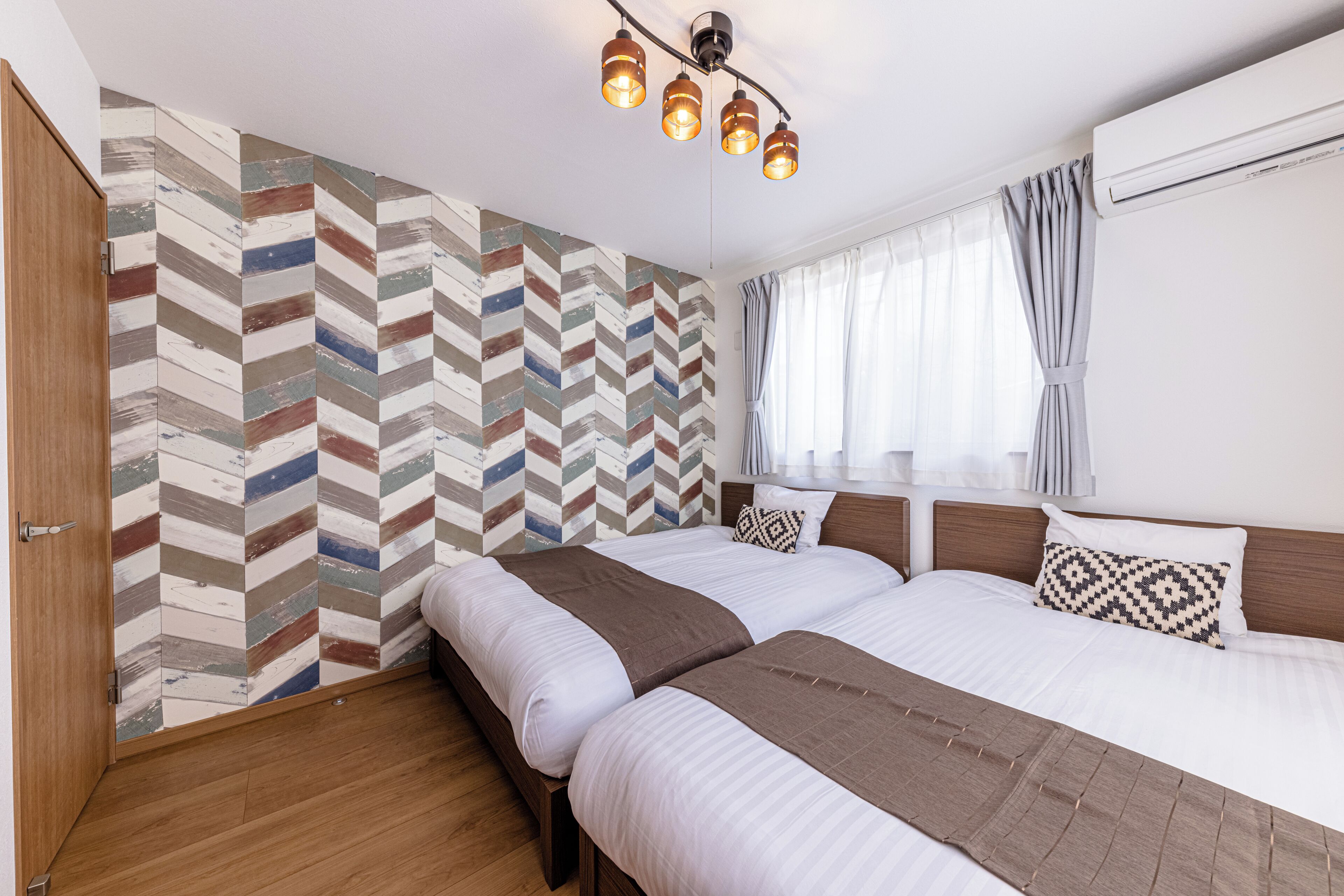 Une chambre d’hôtel avec deux lits, un mur orné d’un motif en chevrons, un plancher en bois et un luminaire au plafond.