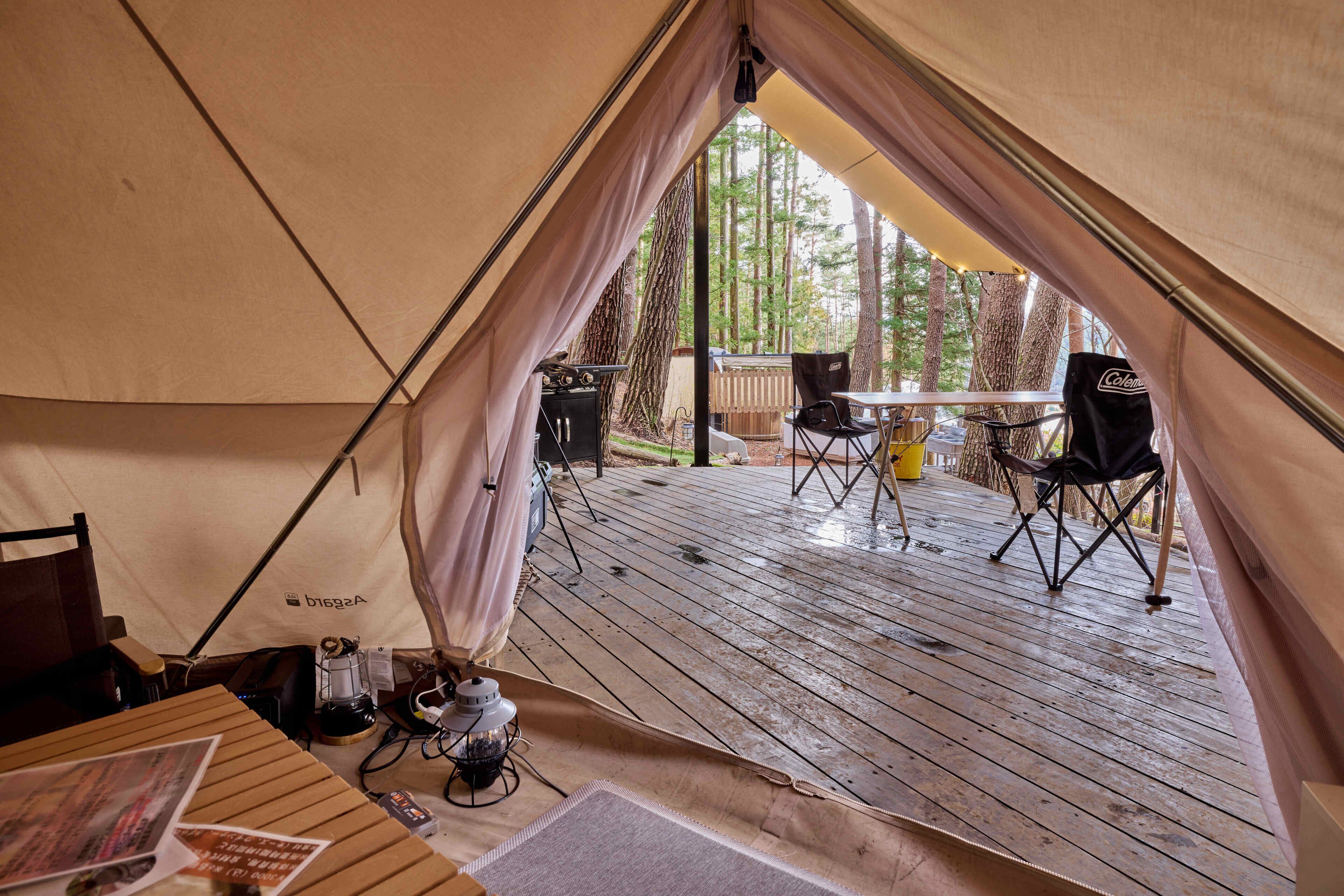 Un espacio para acampar con carpas, una terraza de madera, una mesa, sillas y una silla Coleman.