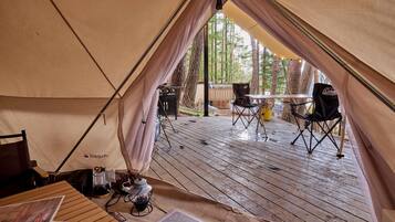 Un espacio para acampar con carpas, una terraza de madera, una mesa, sillas y una silla Coleman.