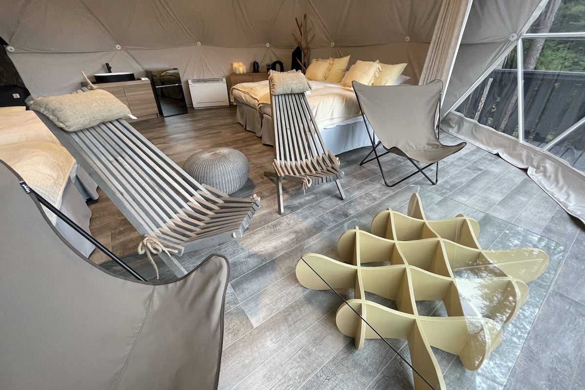 A tent-style room with a bed, lounge chairs, a small table, and a window.
