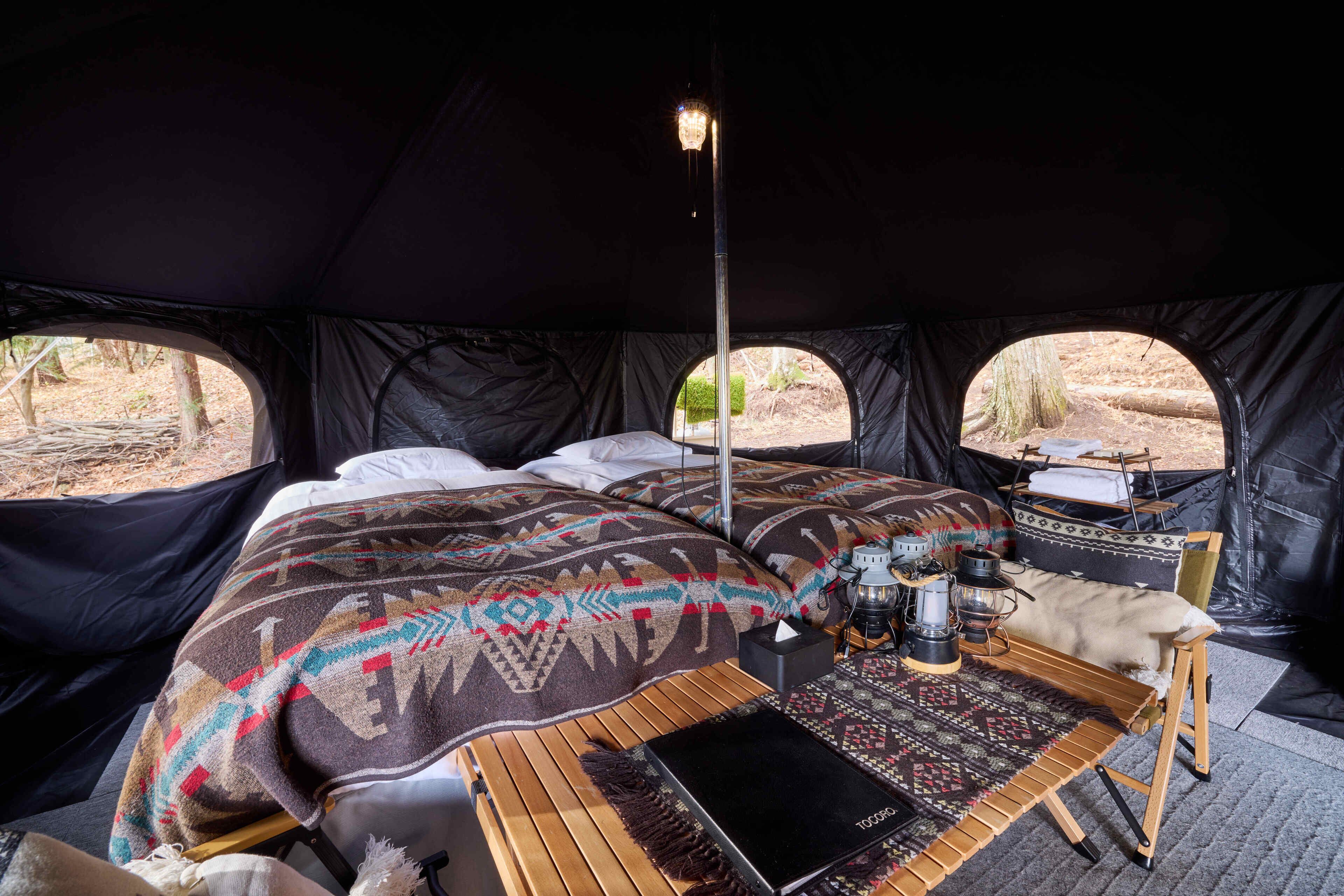 A tent with a bed, a table with a lantern, and a view of the outdoors.