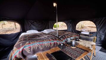 A tent with a bed, a table with a lantern, and a view of the outdoors.