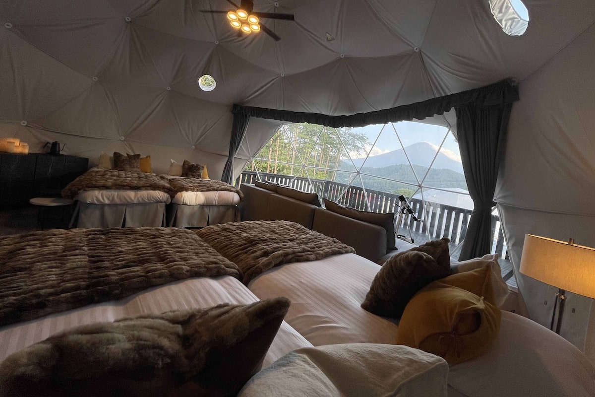 A cozy tented accommodation with a bed, pillows, a small table, and a lamp.
