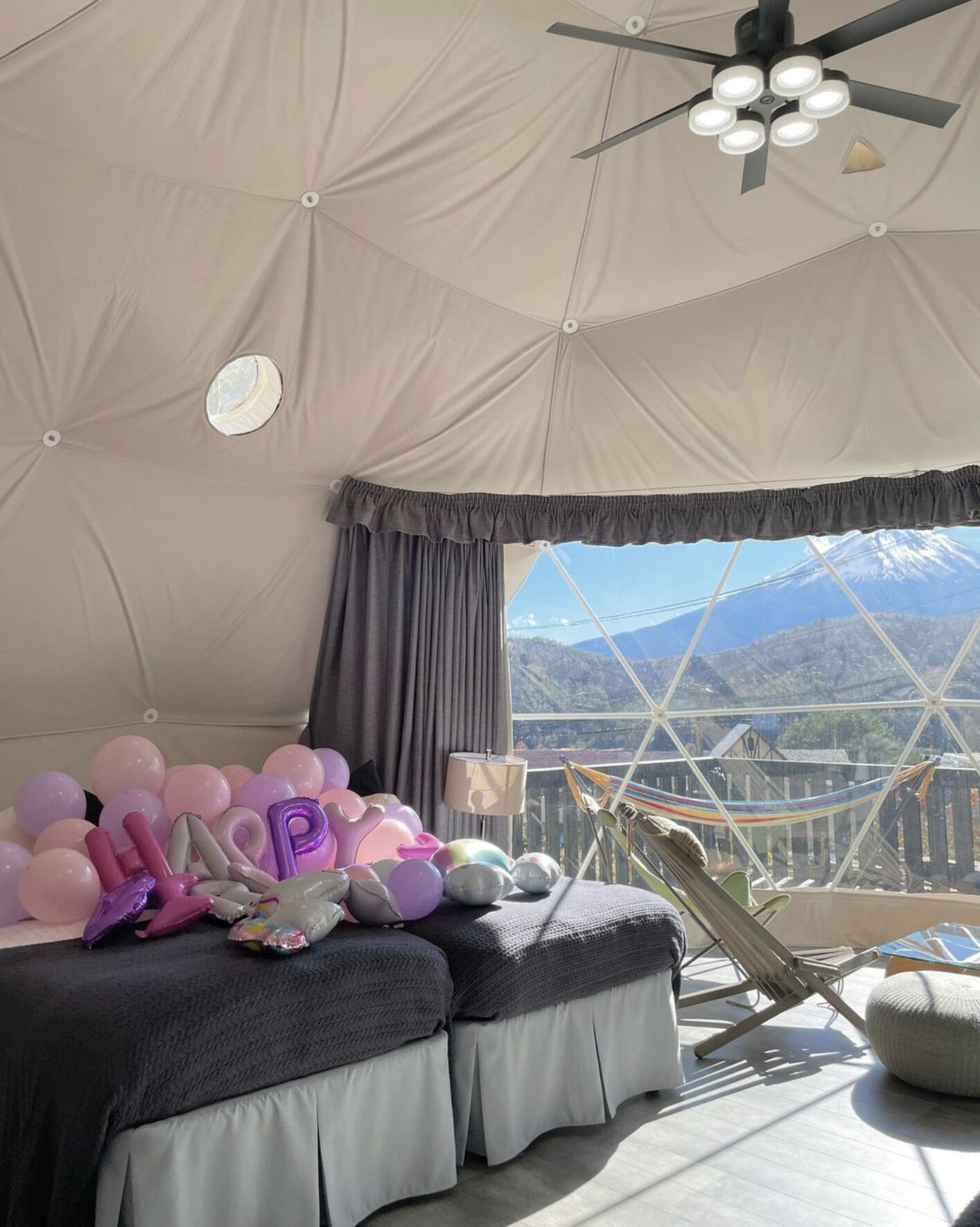 A tented room with a bed, a hammock, and a view of mountains.