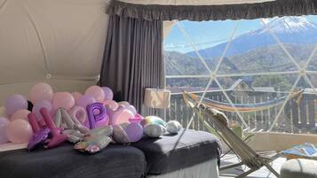 A tented room with a bed, a hammock, and a view of mountains.