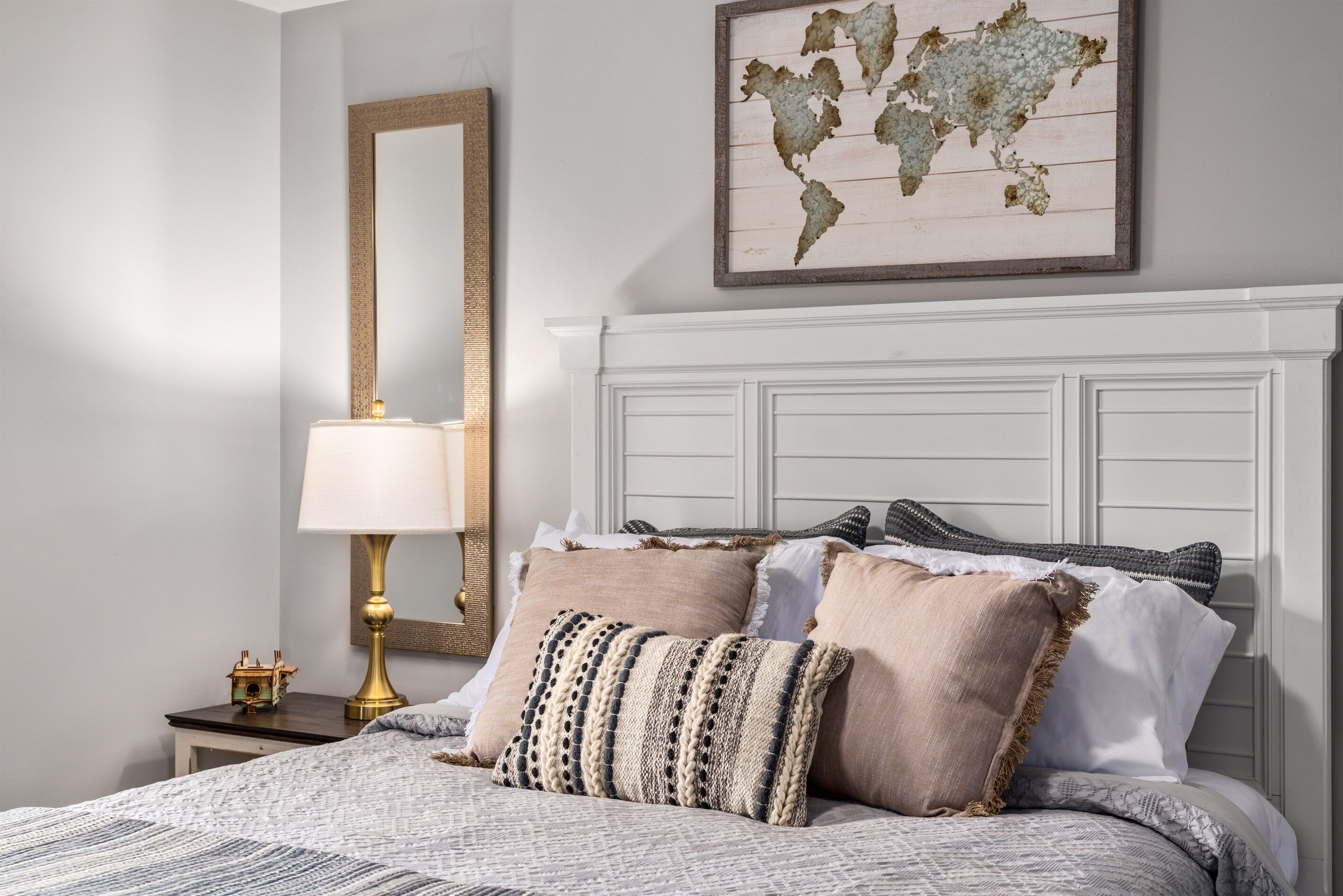 A neatly made bed with a patterned bedspread, a lamp, and a world map on the wall.