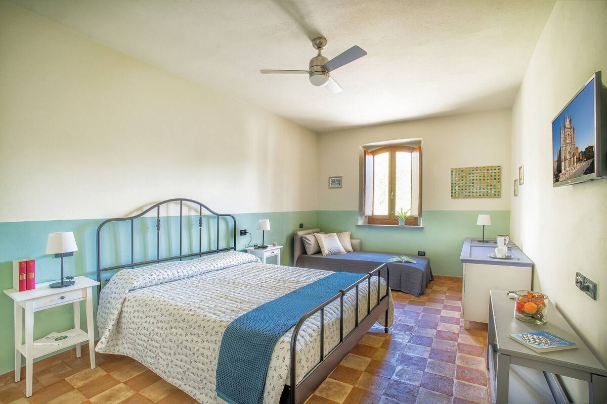 A bedroom with a bed, bedside tables, a desk, a chair, a window, and a ceiling fan.