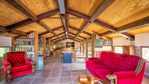 A spacious reading room with high wooden ceilings, a red velvet sofa, a red armchair, and a wooden coffee table. - Torrenova di Assisi Country House (Assisi)