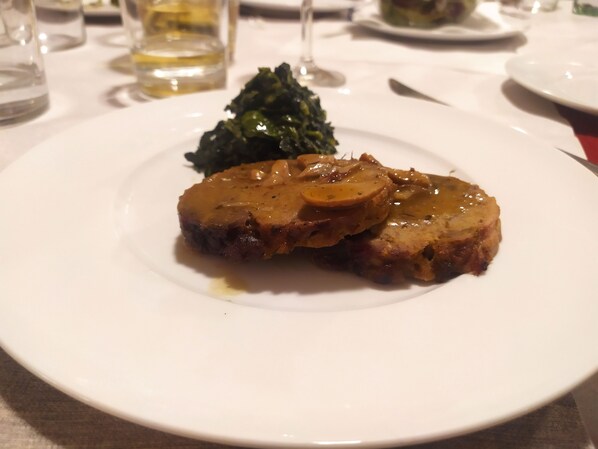 A plate with a piece of meat topped with a brown sauce and a slice of apple, accompanied by a small portion of green vegetables. - Torrenova di Assisi Country House (Assisi)