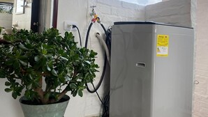 Ein kleiner Kühlschrank, ein Blumentopf und ein Wasserhahn auf Fliesen.