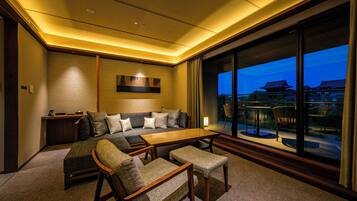 A modern hotel room with a sofa, chairs, a table, and a large window with a view of traditional buildings.