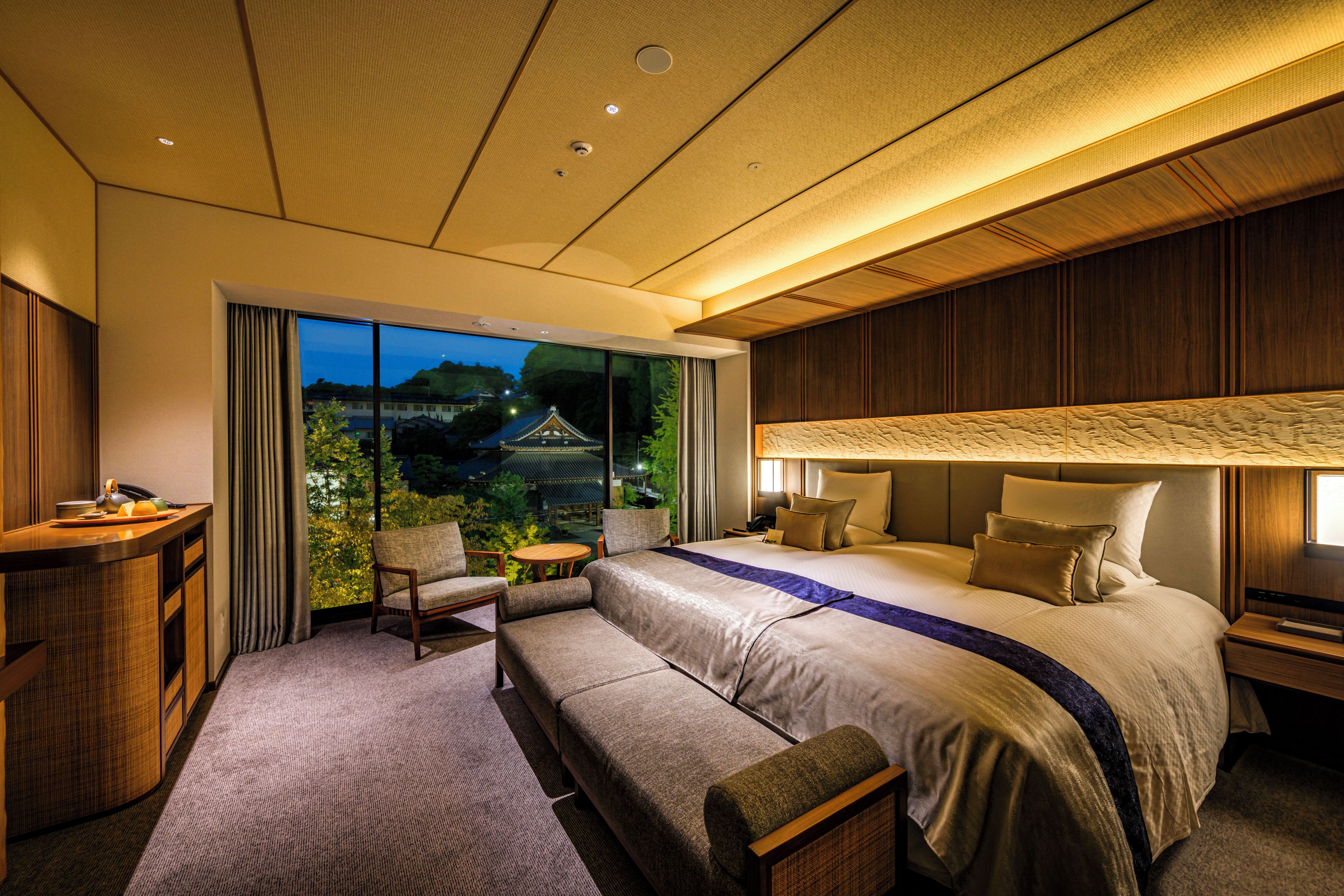 Ein modernes Hotelzimmer mit einem großen Bett, einer Sitzecke, einem Schreibtisch und Blick auf ein traditionelles Gebäude.