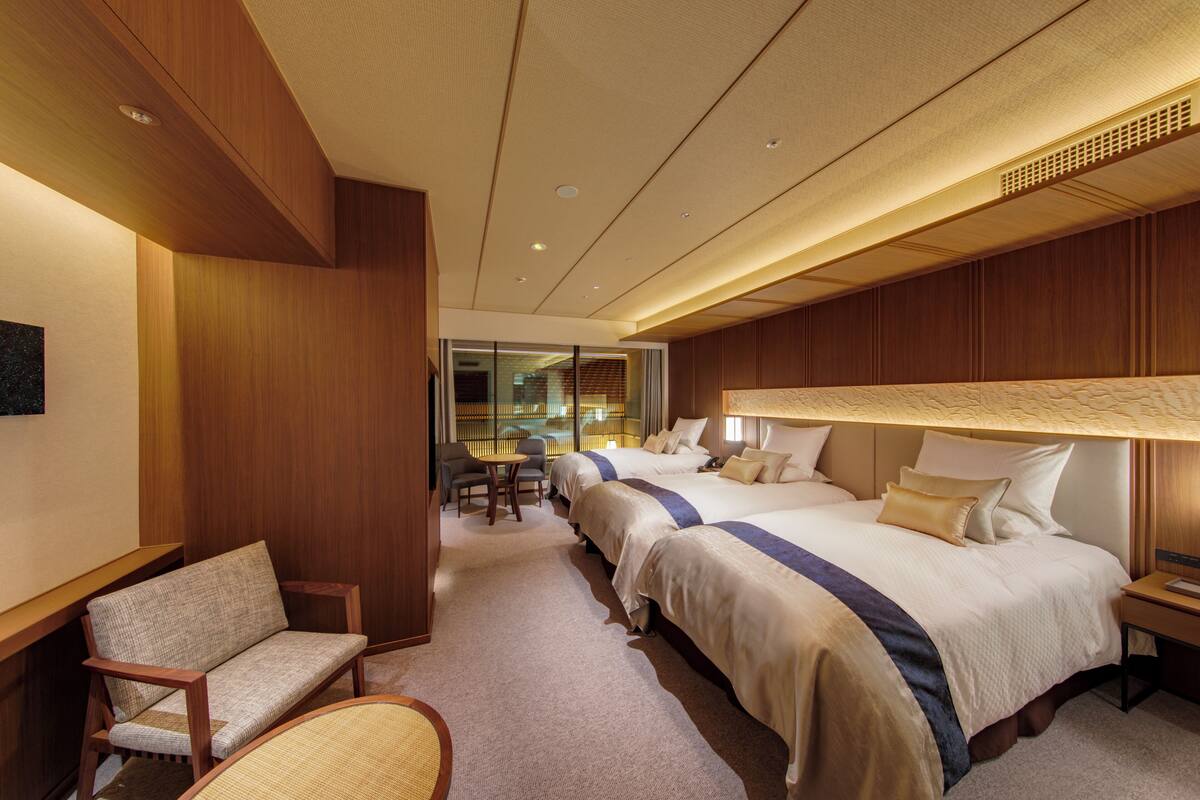 A hotel room with two beds, a sitting area with a chair, and a small table.