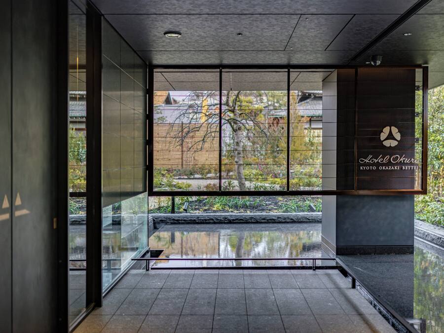 A modern hotel lobby with a glass partition, a water feature, and a sign for Hotel Okura.