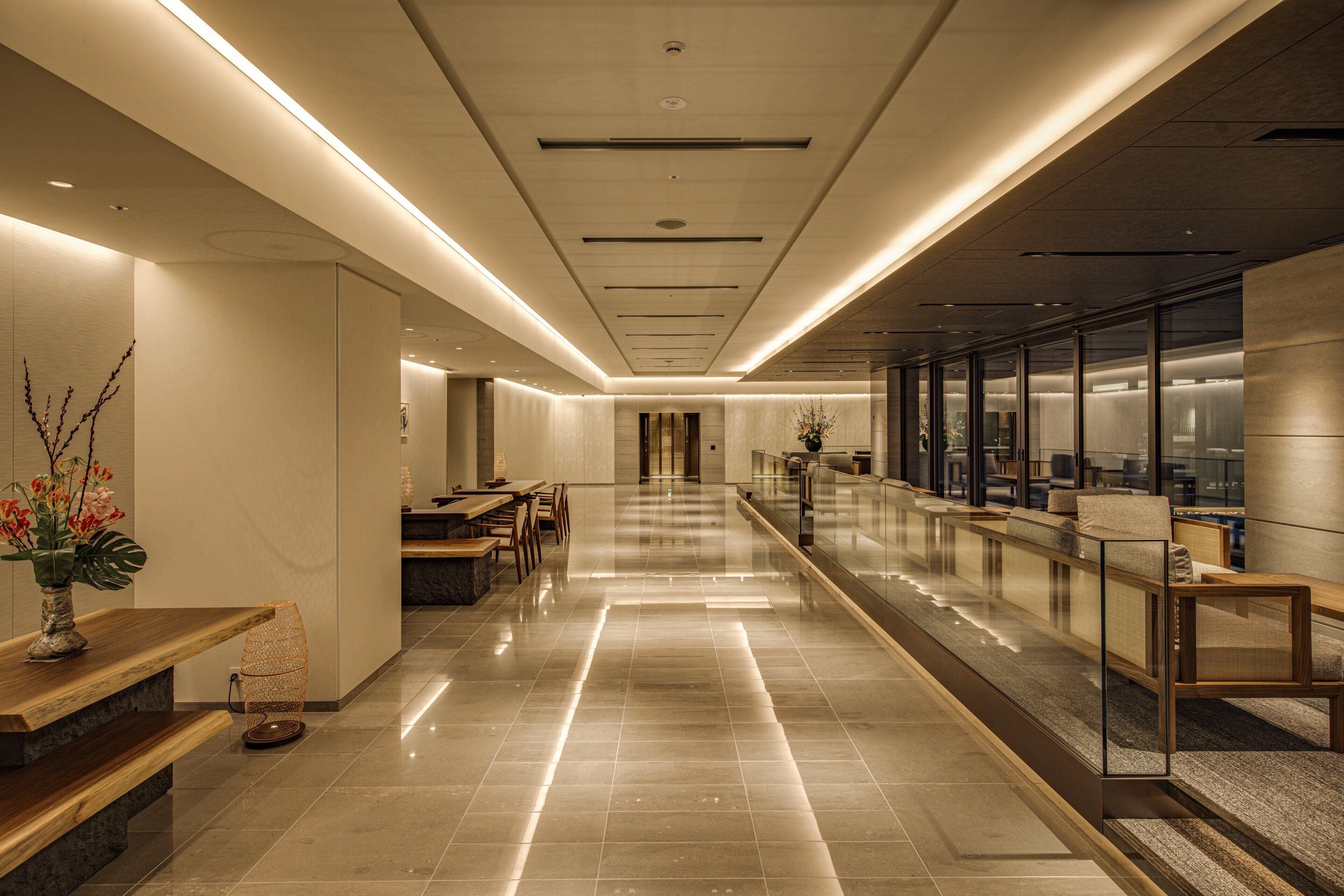 A modern hotel lobby with a long reception desk, seating area, and a glass railing overlooking the lobby.