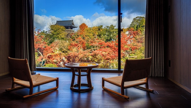 A room with two rocking chairs and a small table, large windows with a view of autumn trees and a traditional building. - Hotel Okura Kyoto Okazaki Bettei (Kyoto)