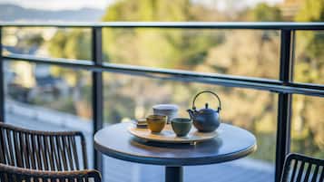 A round table with a teapot, cups, and bowls on a balcony overlooking a scenic view.