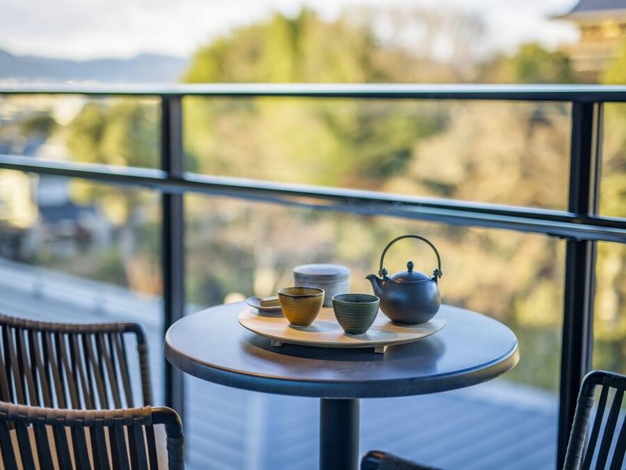 Une table ronde avec une théière, des tasses et des bols, placée sur un balcon donnant sur un paysage magnifique.