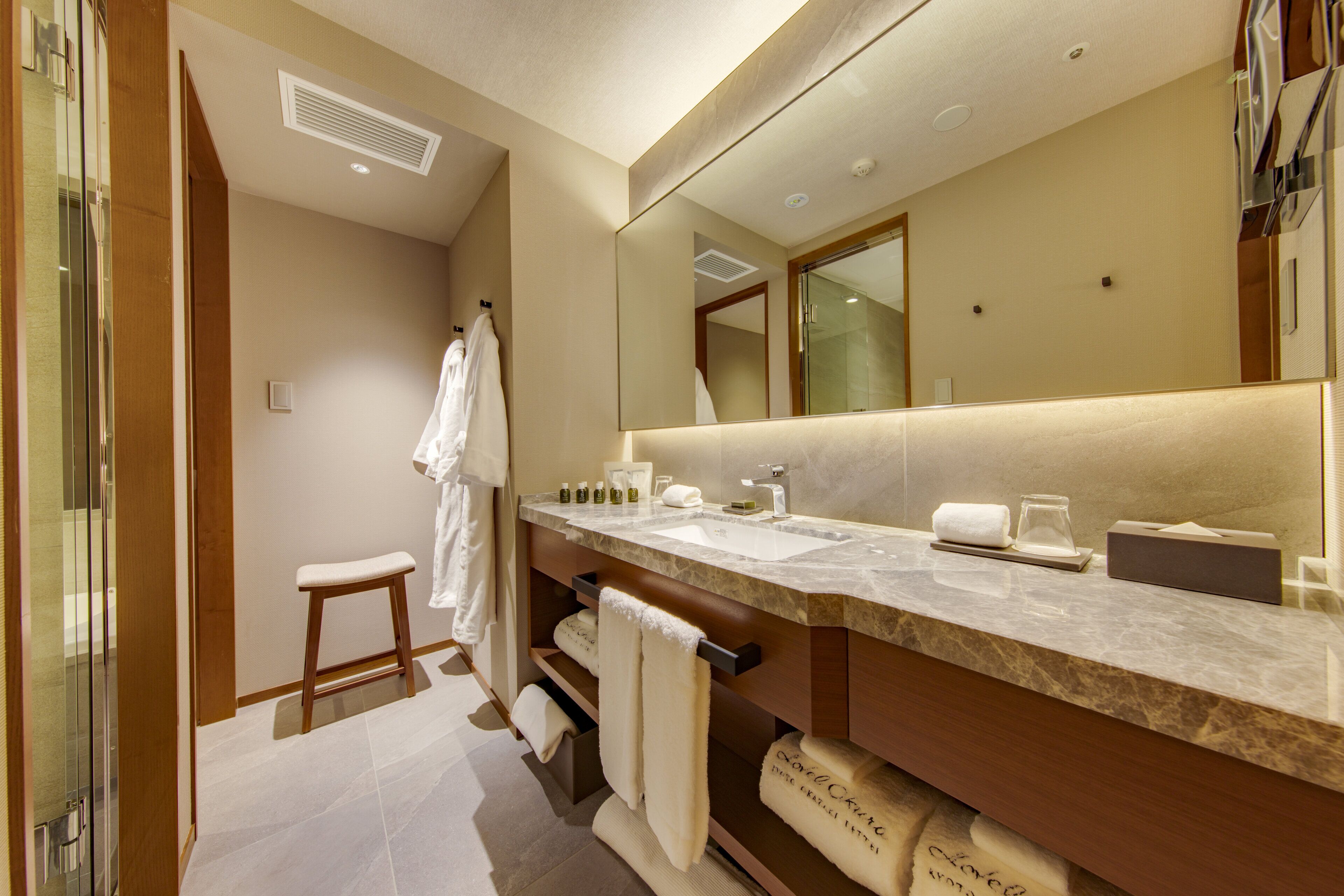 A modern bathroom with a large mirror, a vanity with a marble countertop, and a shower area.
