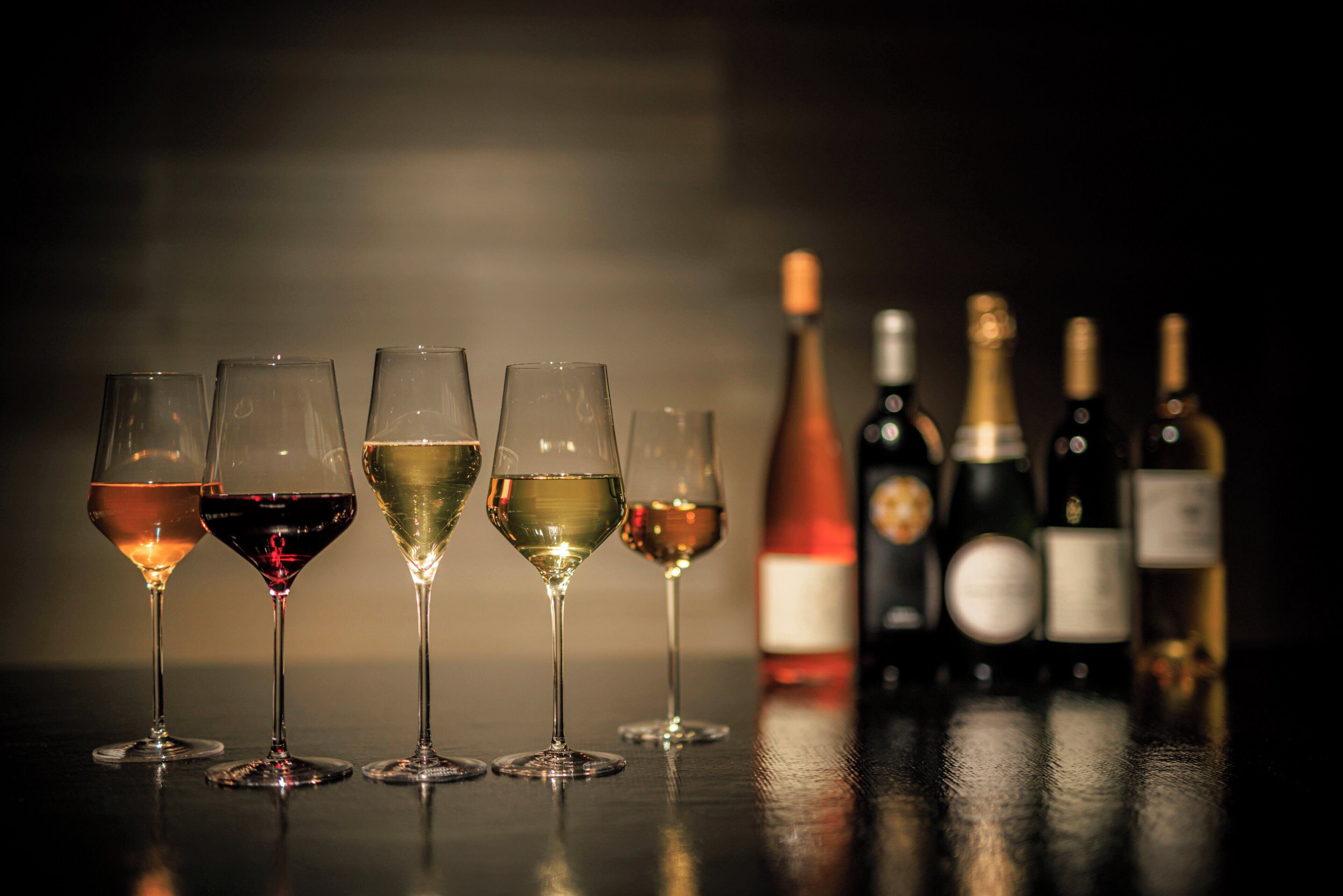A row of wine glasses and bottles on a reflective surface.
