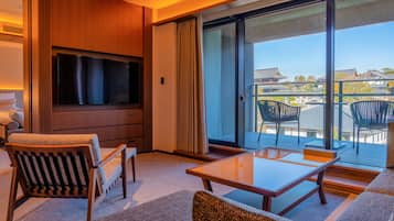 A hotel room with a flat-screen TV, a sofa, a table, and a balcony with chairs.