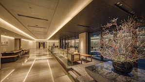 A modern hotel lobby with a long reception desk, seating area, and a large potted plant. - Hotel Okura Kyoto Okazaki Bettei (Kyoto)