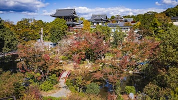 A traditional Japanese temple complex with multiple buildings, a small bridge, and a pond surrounded by autumn-colored trees.