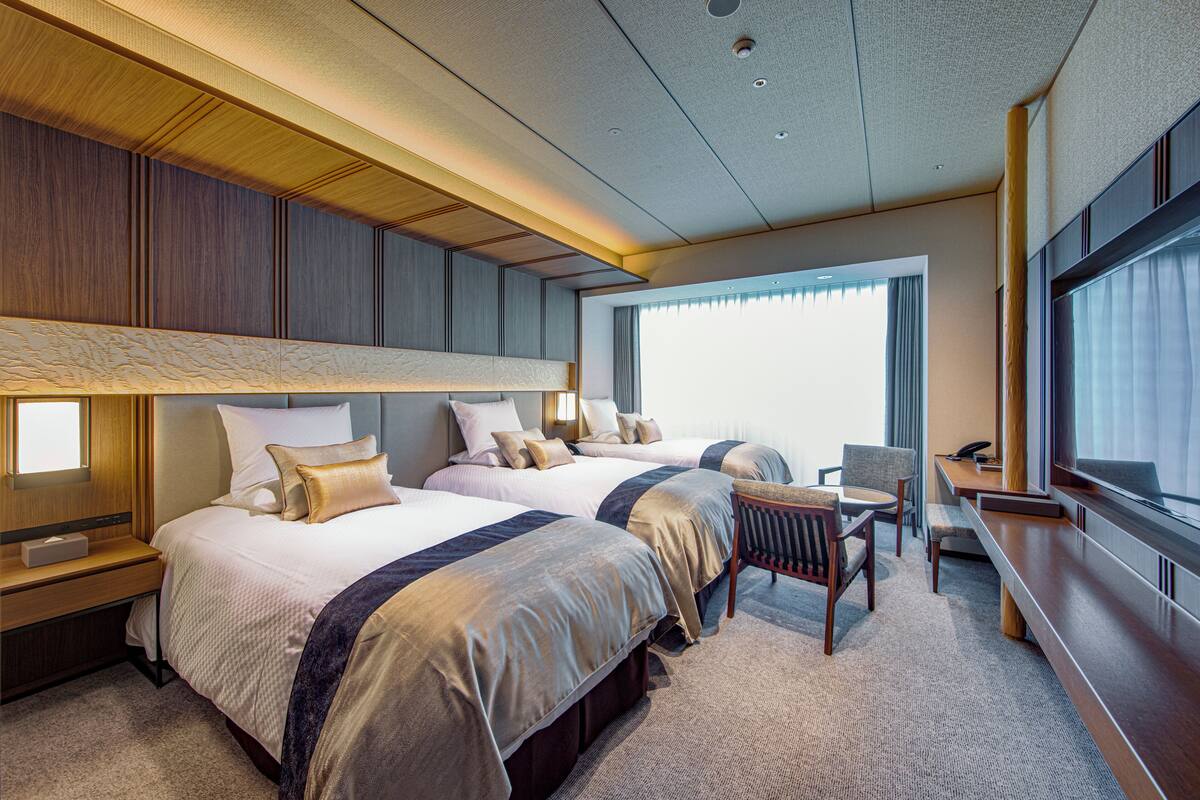 A hotel room with two beds, a desk, a chair, and a large window.
