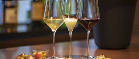 A bar setting with three glasses of wine, one being filled with a white wine, and a bottle of champagne being poured. There are small plates with food items on the table.
