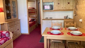 Una habitación compacta con literas, una mesa de comedor para dos personas y un pequeño espacio de cocina.