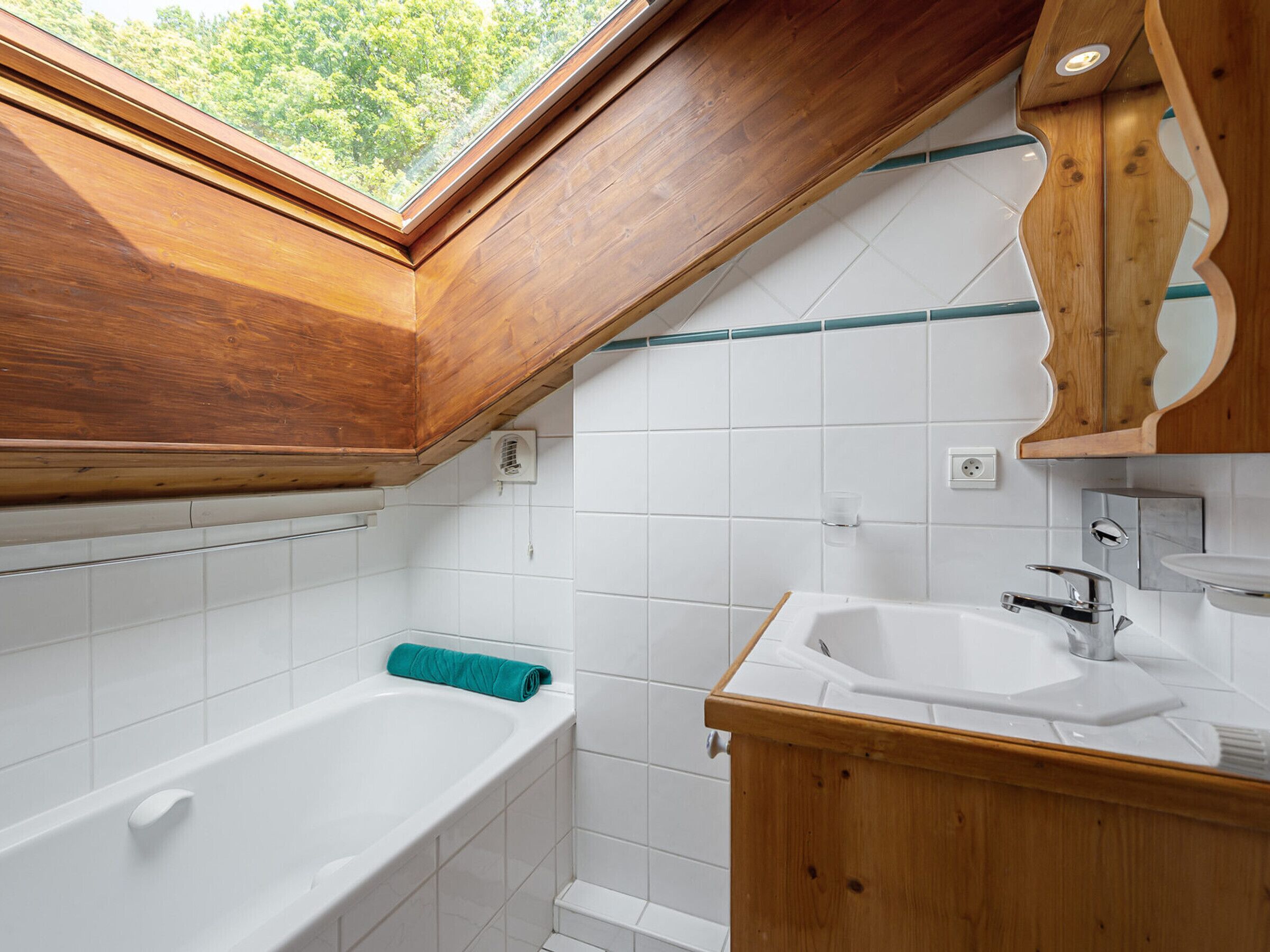 Un bagno con finestra a lucernario, una vasca, un lavandino e mobili in legno.