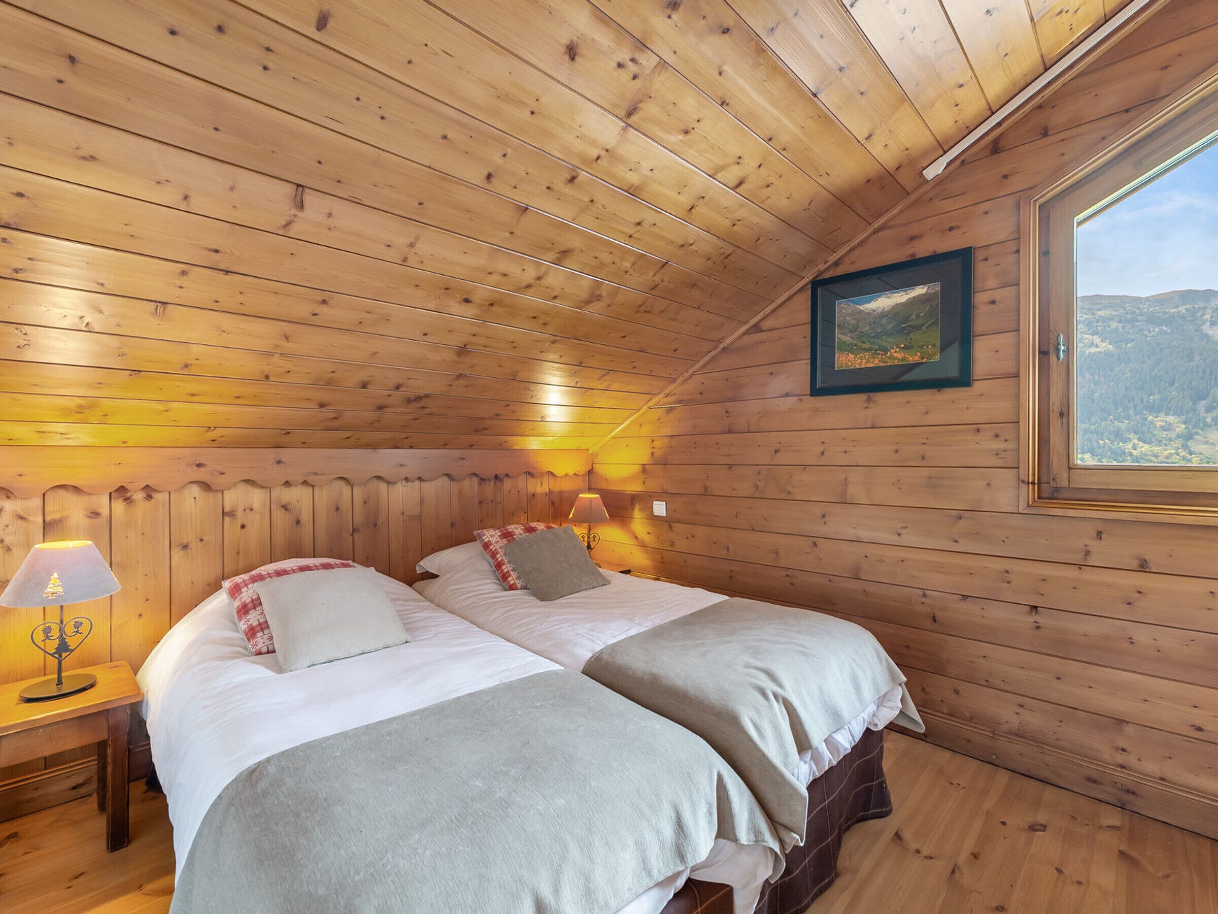 A wooden cabin bedroom with two beds, a nightstand, a lamp, and a framed picture on the wall.