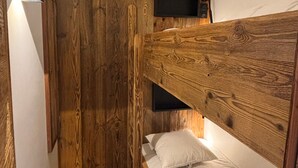 A bedroom with a wooden headboard, a single bed with white bedding, and a small TV mounted on the wall. - Stunning 8-person apartment, central location, pets allowed (Avoriaz)