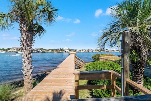 A wooden boardwalk leading to a waterfront with palm trees and a clear blue sky.