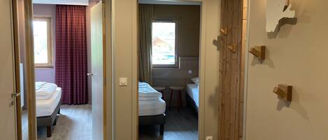 A hotel room with a bed, a small stool, a window with curtains, and a wooden wardrobe.