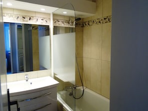 Een badkamer met een wit wastafel, een spiegel, een douche en beige betegelde wanden.