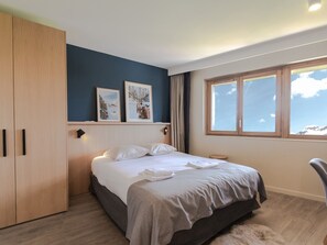 Ein Schlafzimmer mit Bett, Kleiderschrank, Fenster mit Aussicht und zwei gerahmten Bildern an der Wand.