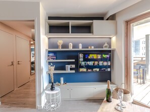 A modern interior with a built-in TV shelf, a small round table with a bottle and glasses, and a view of the outside.