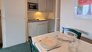 Cocina compacta con microondas, fregadero y lavavajillas, y un comedor con una mesa preparada para dos.