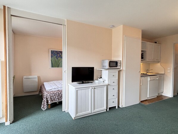 Ein kleines Zimmer mit Bett, Fernseher, Mikrowelle und einer Küchenzeile.
