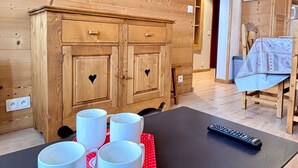 Un meuble en bois doté de poignées en forme de cœur, une table avec quatre tasses blanches et une télécommande posée sur une table noire.