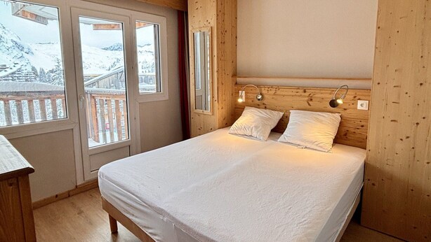 Une chambre à coucher avec une tête de lit en bois, deux lampes de chevet et une grande fenêtre donnant sur un paysage enneigé.